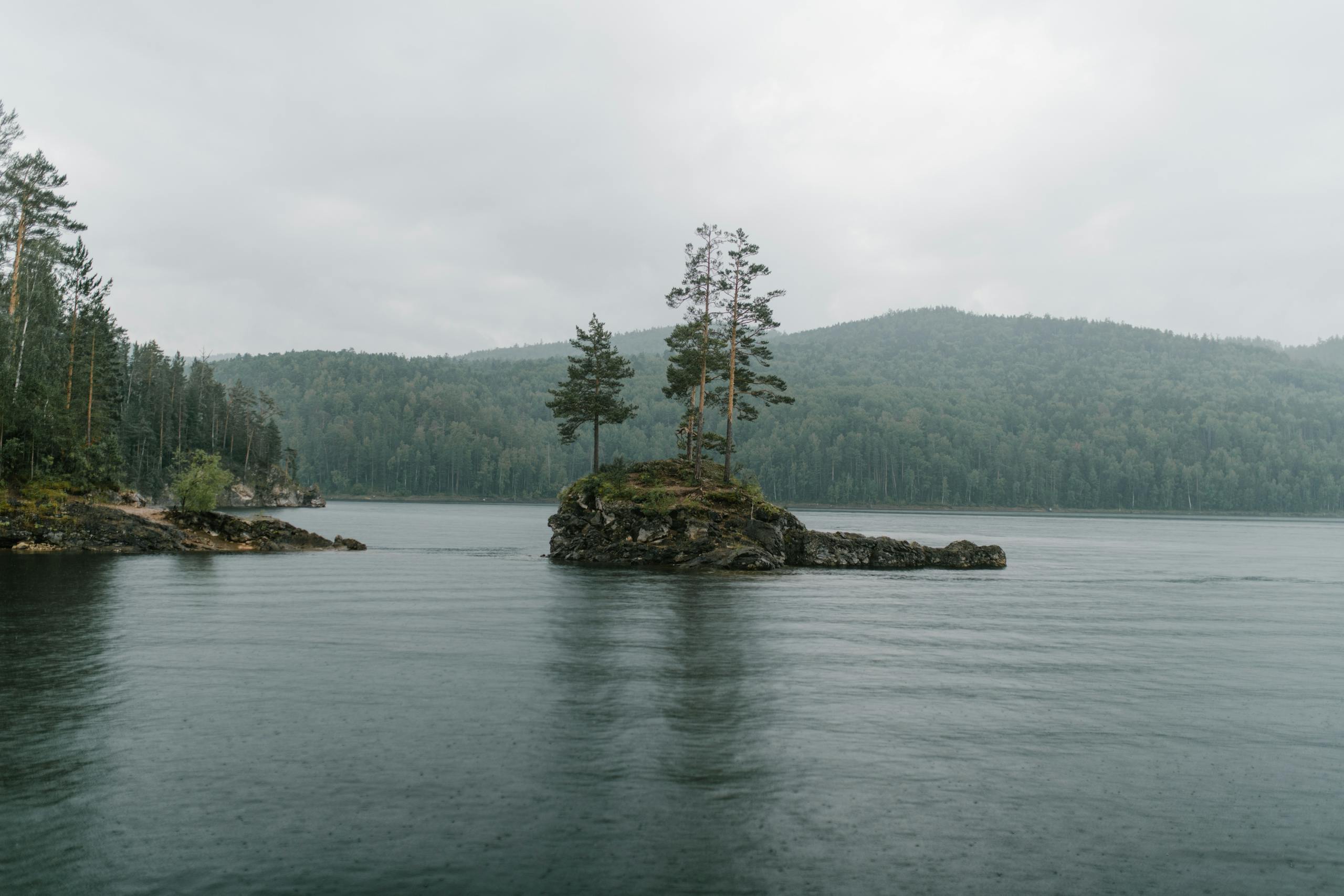 A tranquil island on a misty lake surrounded by lush forests and hills. Captured on a Nikon D850.