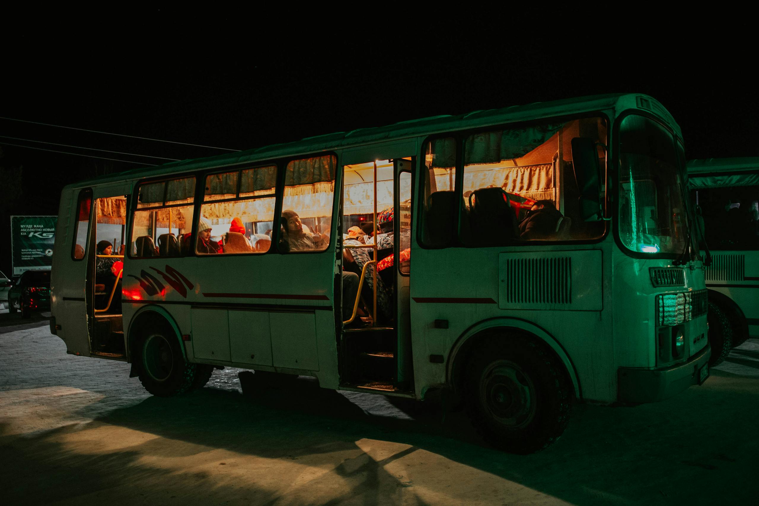 A bus parked at night with passengers visible inside, creating a warm, inviting glow.