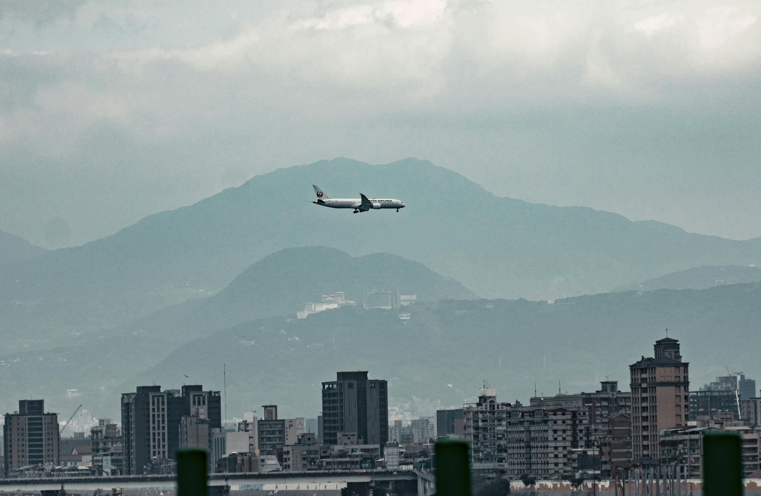 Airplane flying above Taipei skyline and mountains on a cloudy day.