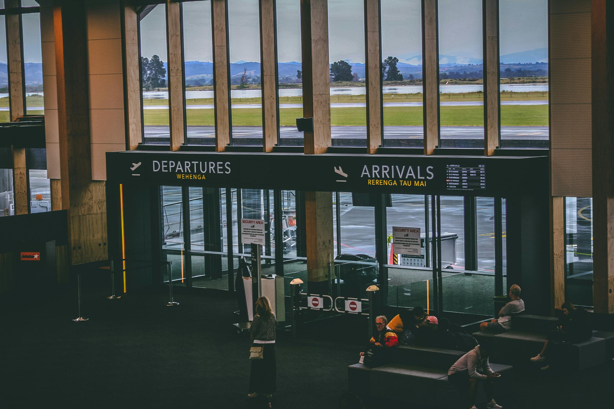 Busy airport terminal area with people, featuring departures and arrivals signs.