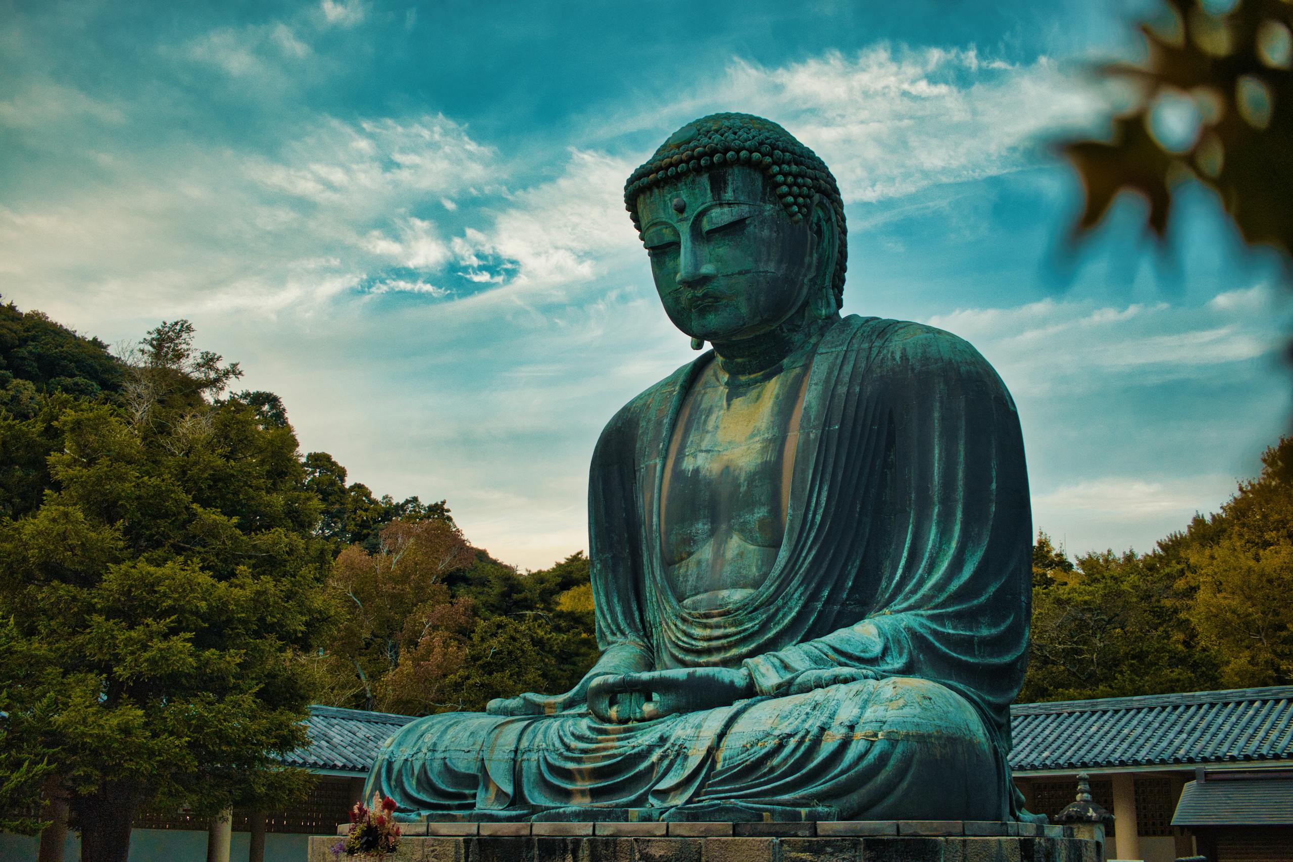 The Great Buddha statue in Kamakura surrounded by lush greenery and a serene sky.
