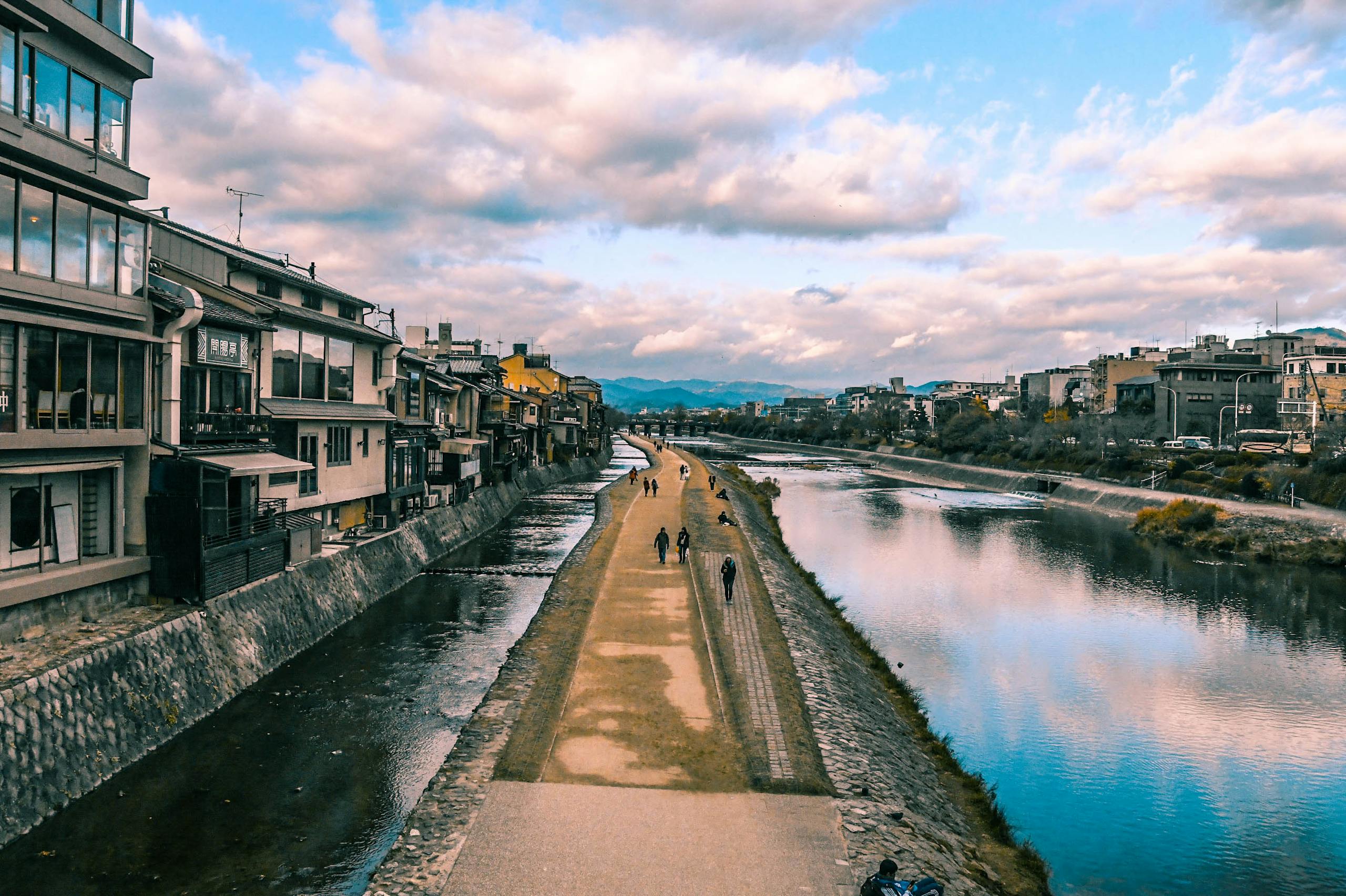 Tranquil view of a riverside pathway in Kyoto with traditional architecture and serene water reflections.