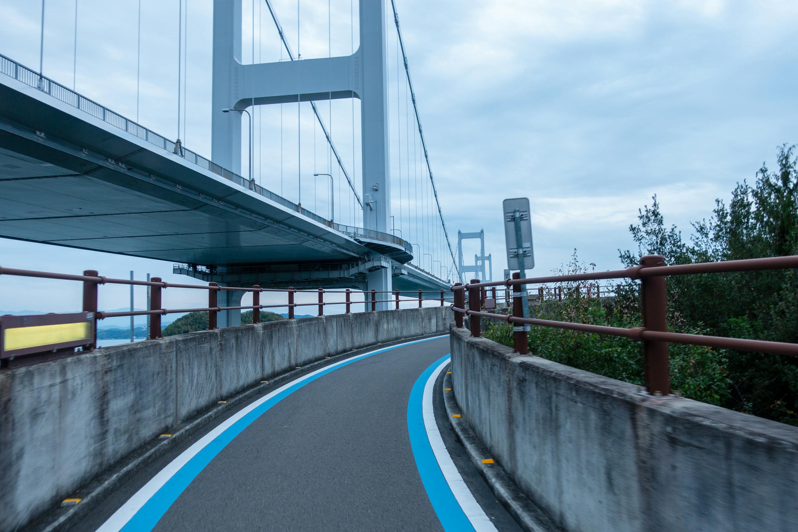 A curved bike lane under the Onomichi bridge in Hiroshima, Japan, during a clear day.