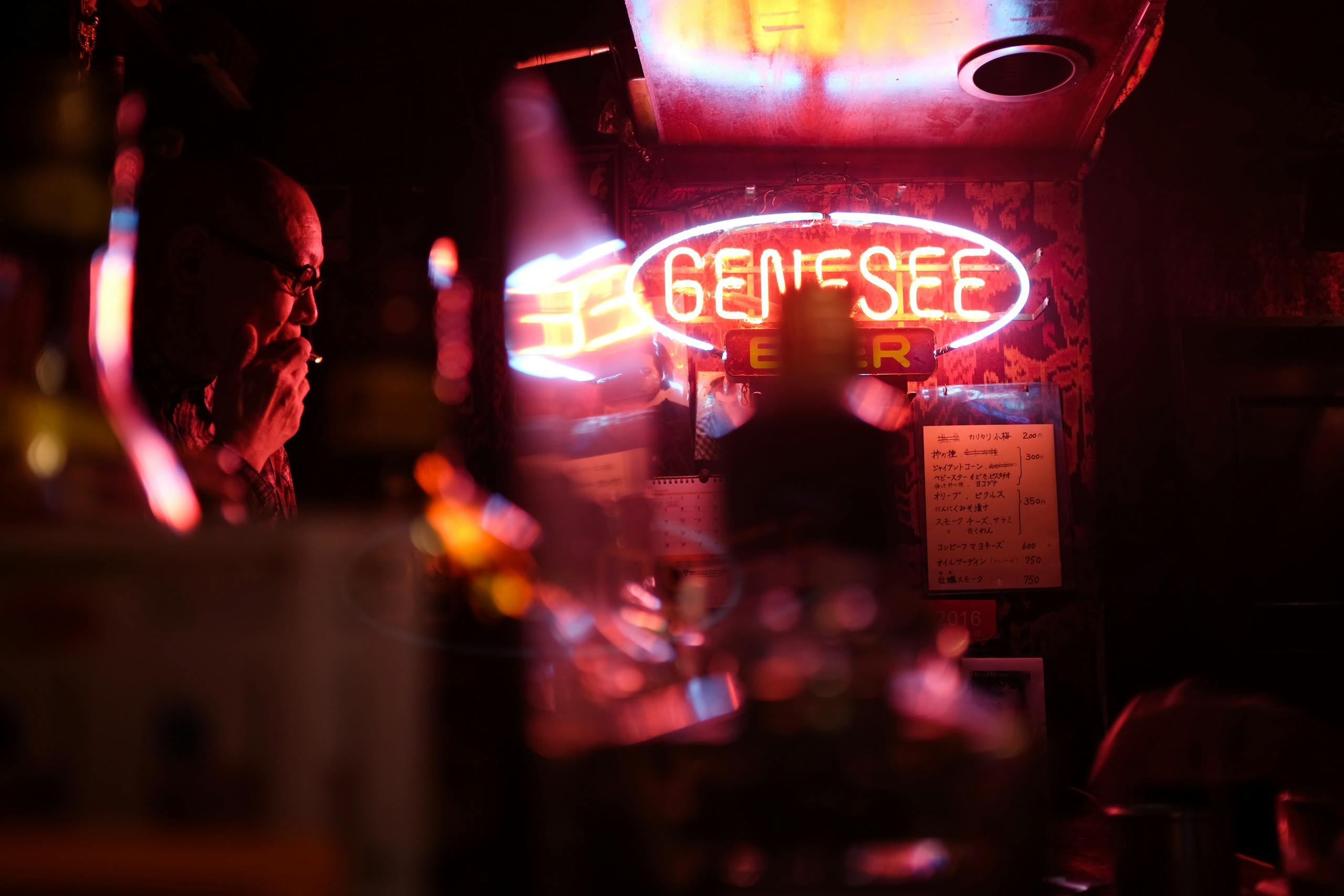 A man smoking in a Tokyo bar under vibrant neon lights creates a moody atmosphere.