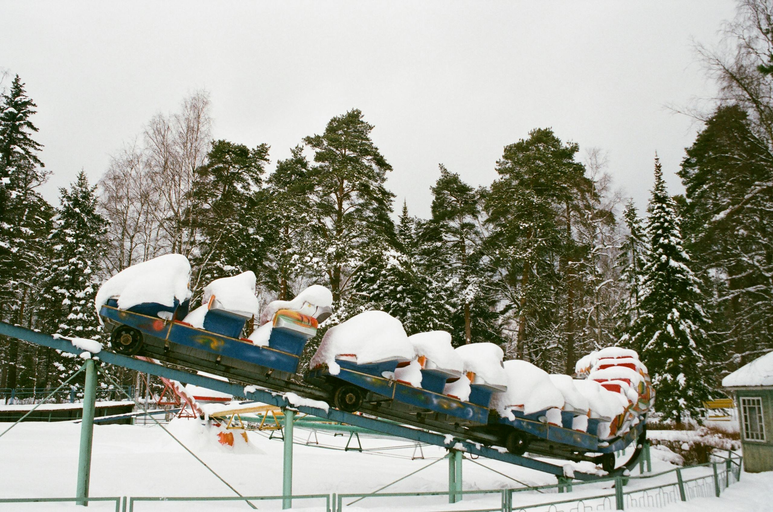 A scenic winter landscape featuring a snow-covered roller coaster surrounded by frosty trees in a snowy park.