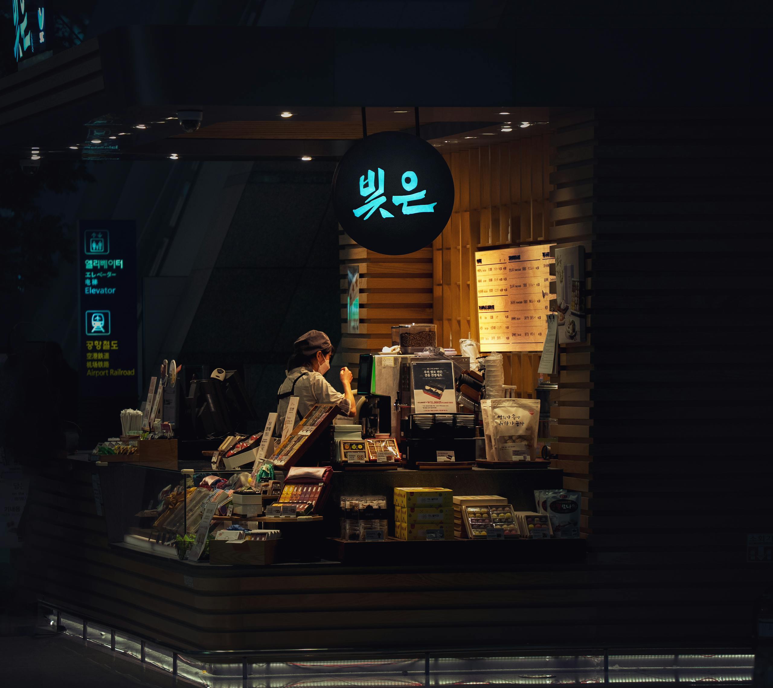A woman working inside a cozy café at night, view through the window.