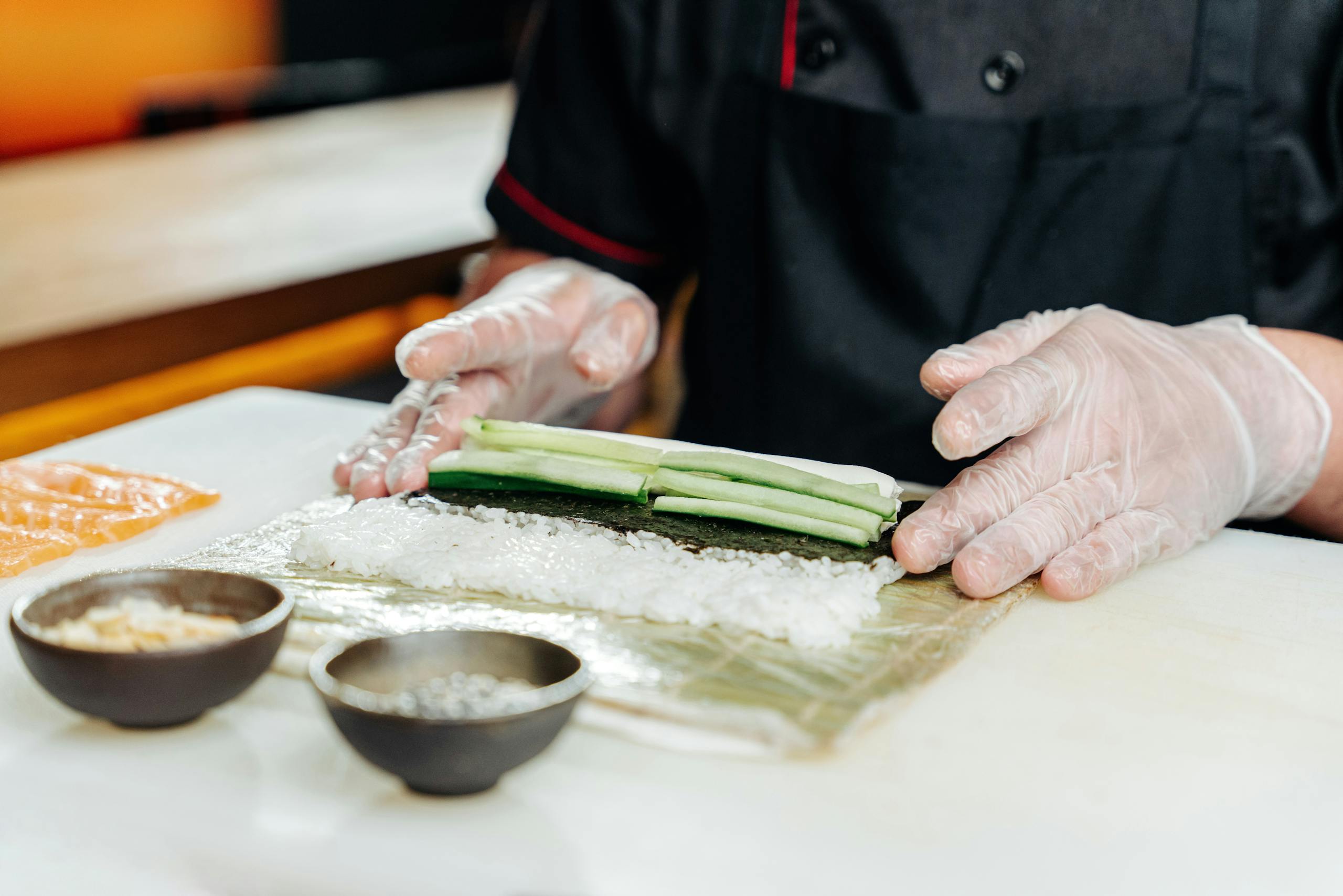 Chef expertly preparing sushi with rice, cucumber, and salmon, showcasing Japanese culinary skills.
