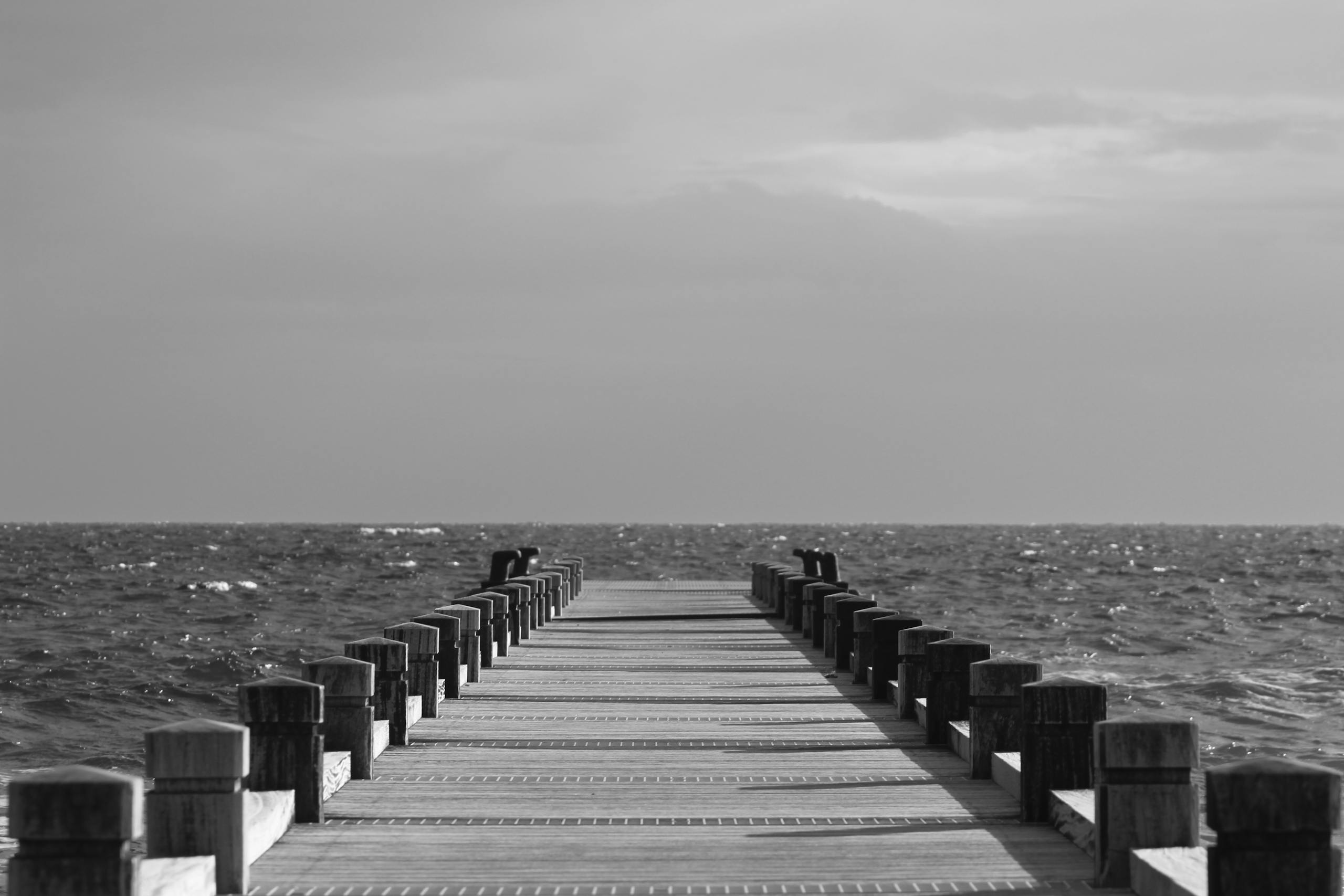 Monochromatic view of a peaceful pier extending into the ocean under a cloudy sky.