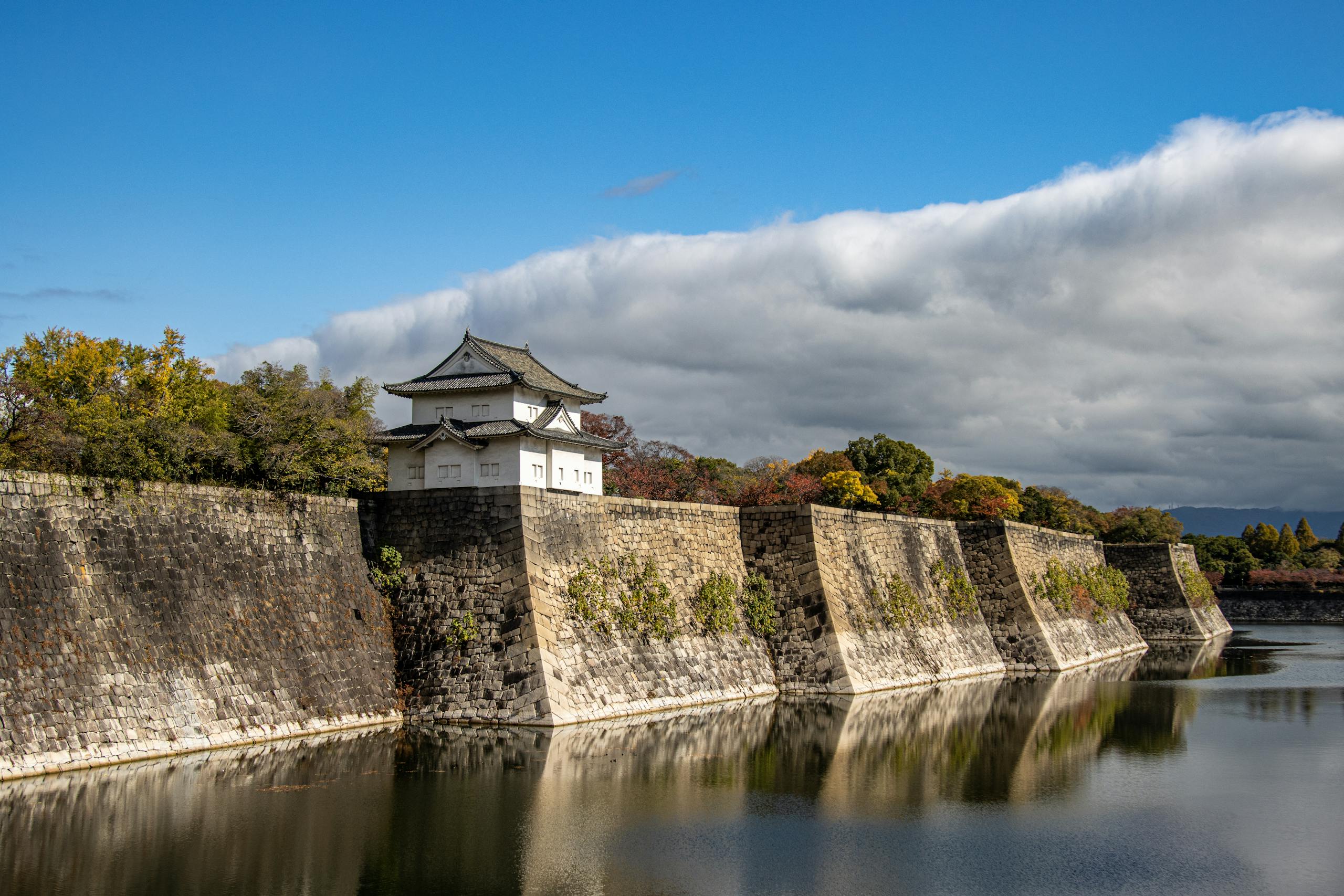 Scenic view of Osaka Castle walls reflecting on the calm moat water under a bright sky.