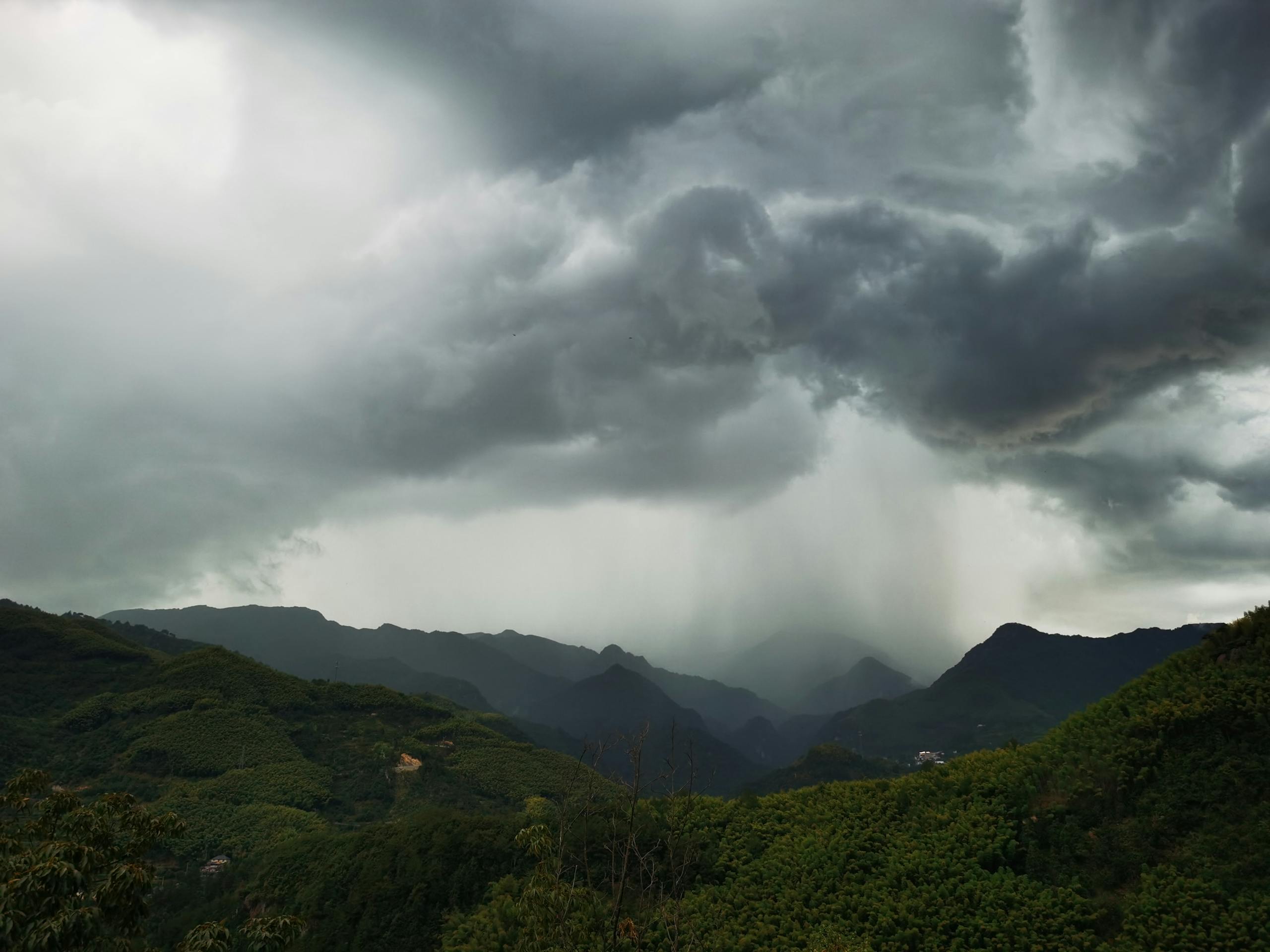 A breathtaking view of dramatic rain clouds over lush green mountains in Hangzhou, China.