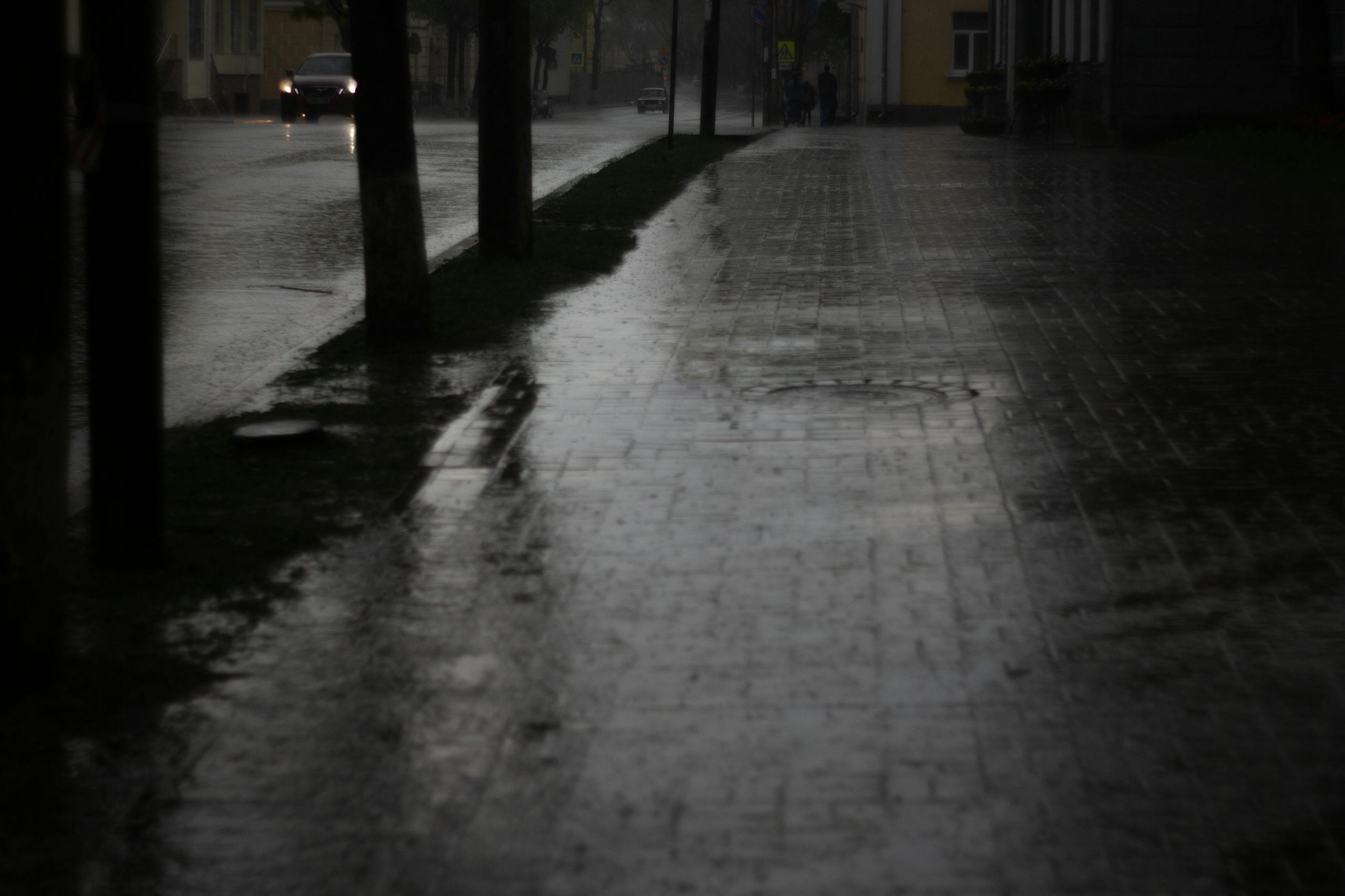 A gloomy and empty city street at dusk, soaked by rain reflecting urban lights.