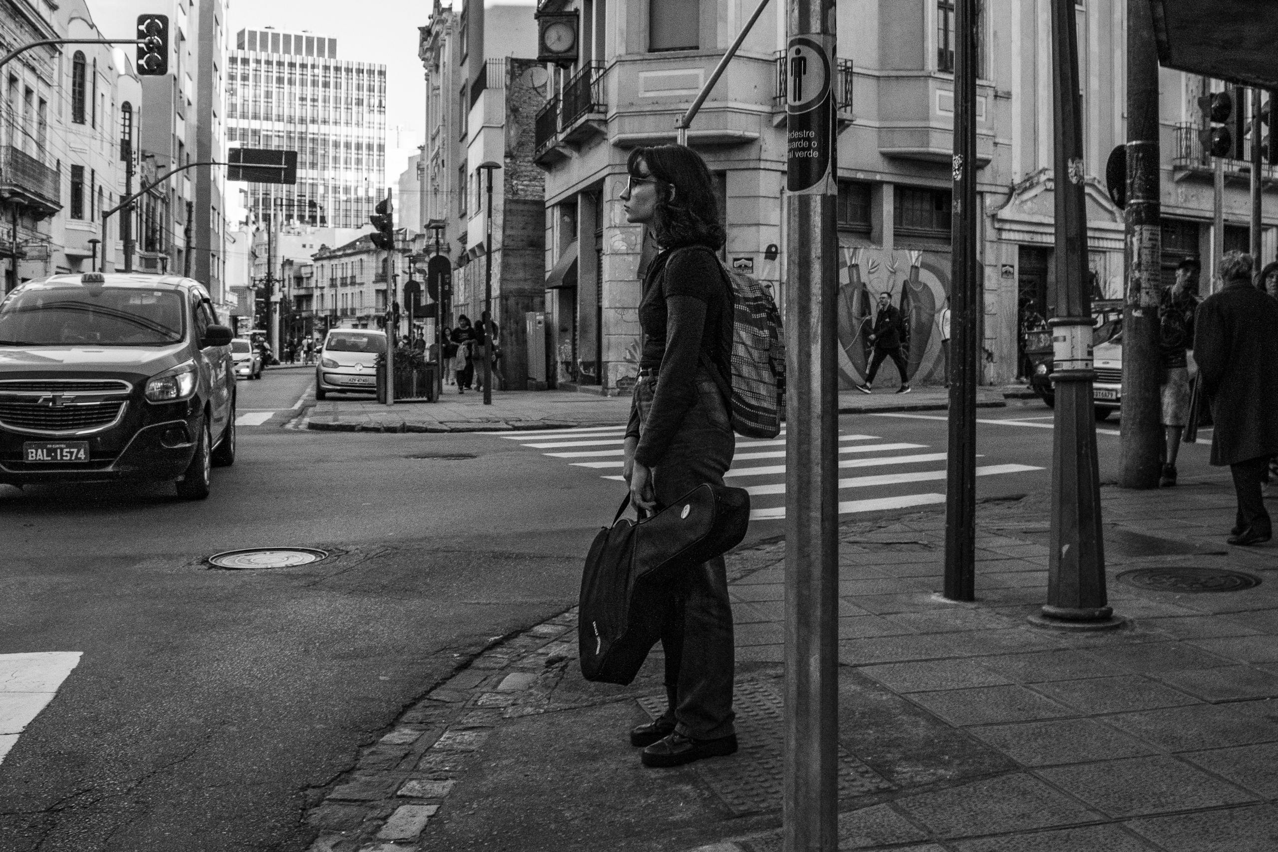 Black and white street scene with a woman waiting at a zebra crossing in an urban setting.