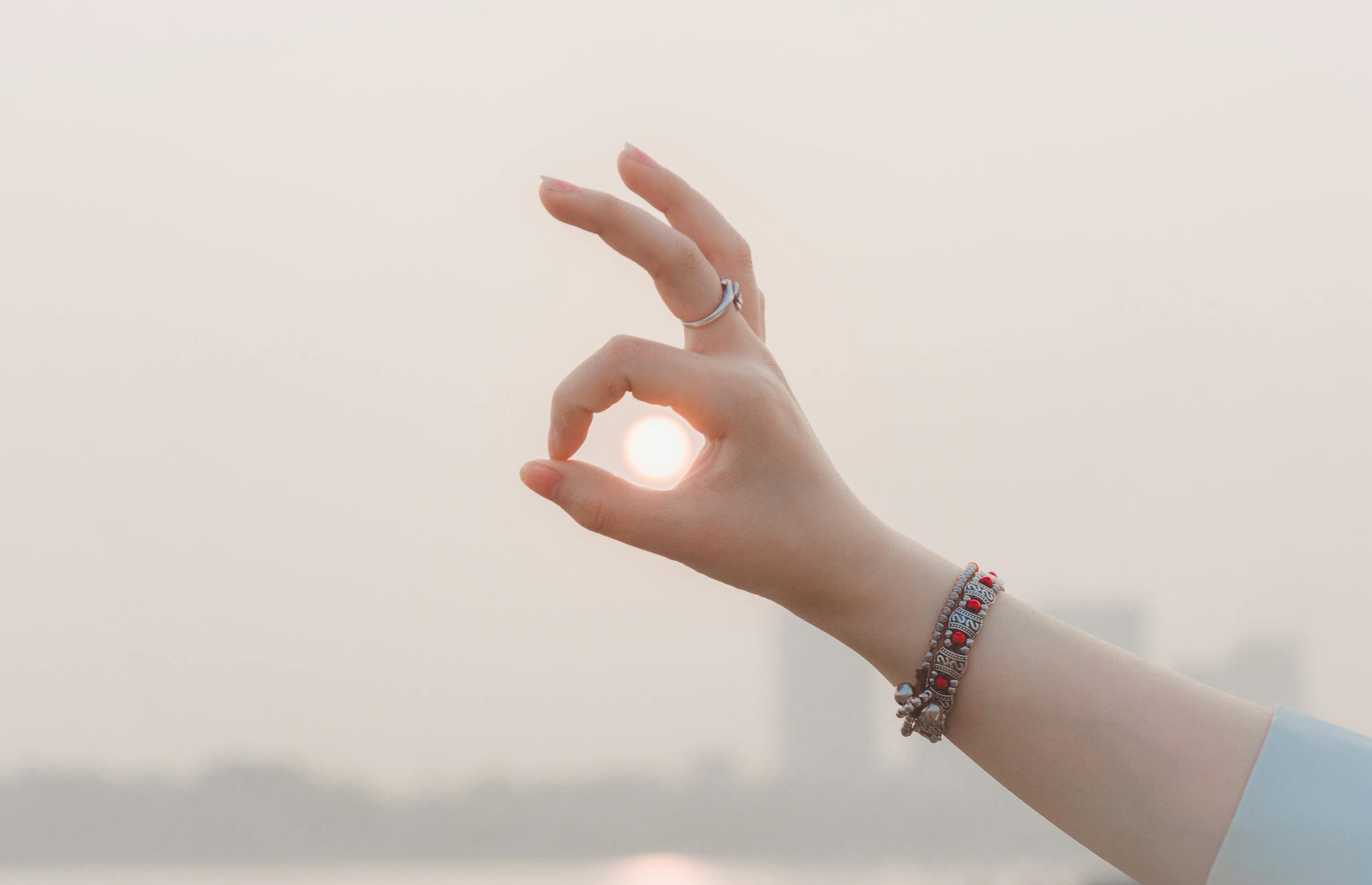 Crop unrecognizable female demonstrating OK gesture while touching glowing sun in evening in town