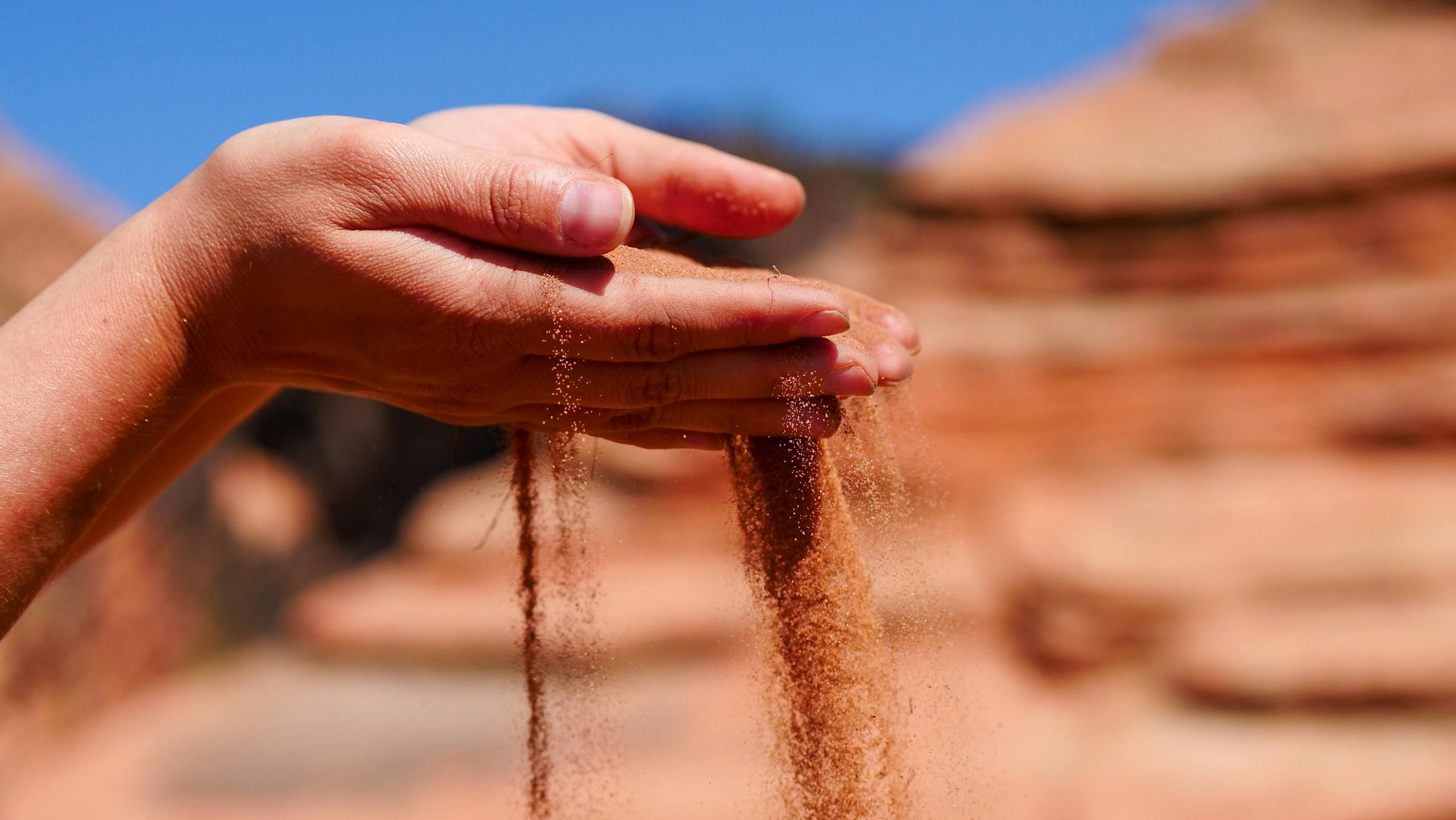 Hands gently pouring sand with blurred desert background, capturing tranquility and time passage.