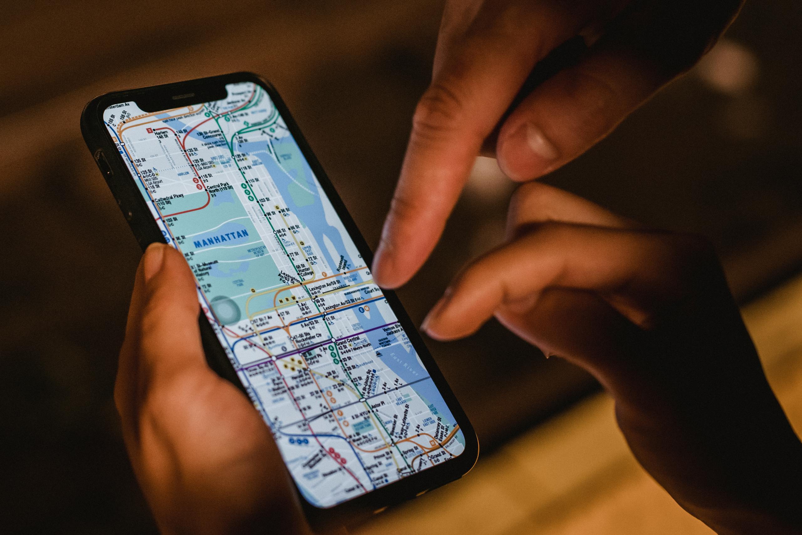 Unrecognizable couple examining map of modern city on screen of smartphone while standing on dark street in city with blurred background