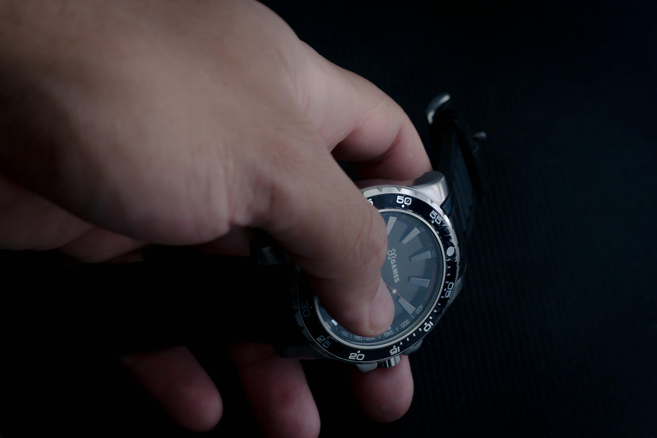 A hand holding a sleek analog wristwatch on a dark background.