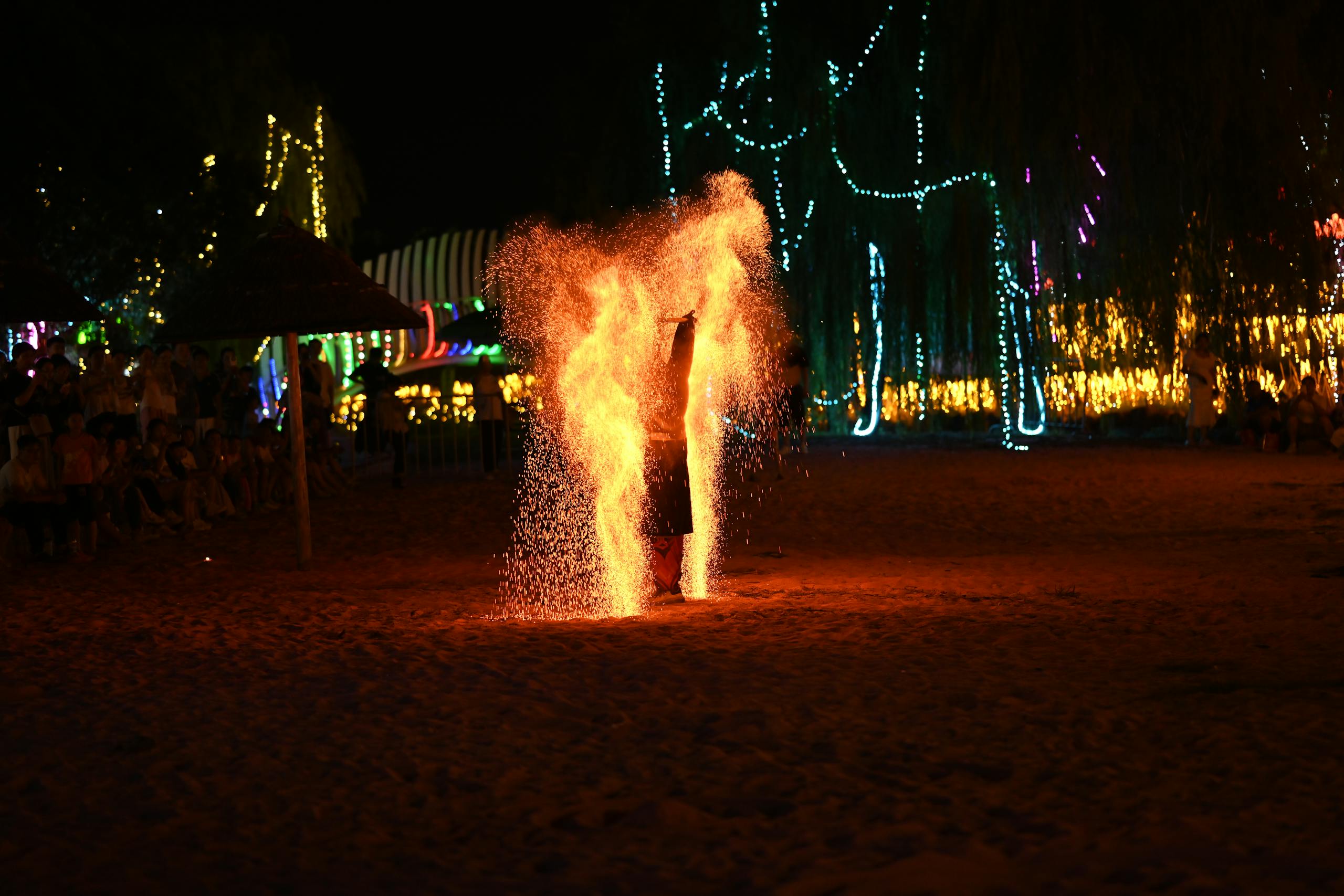 A mesmerizing fire performance at a night festival on the beach, surrounded by colorful lights and spectators.