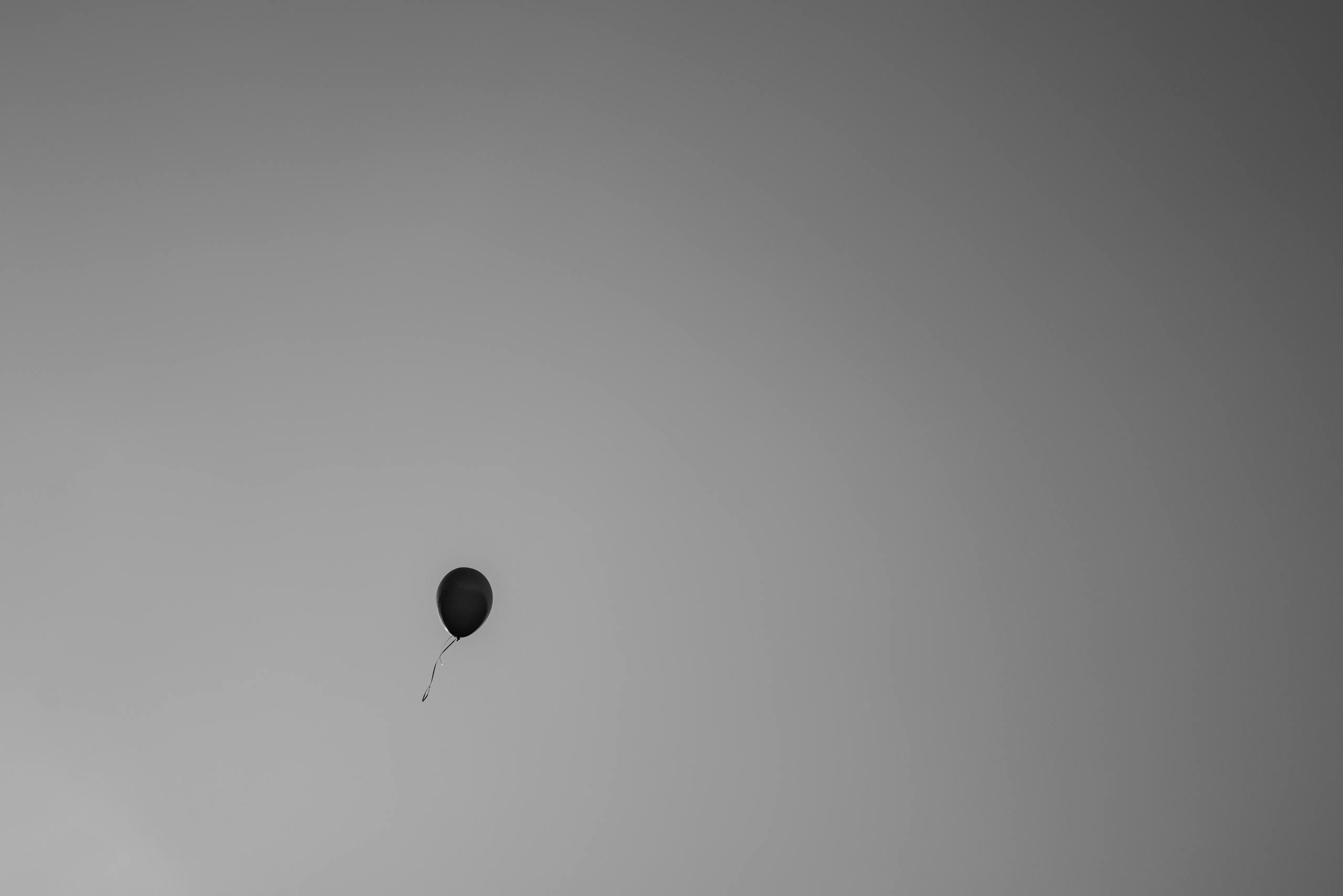 A single black balloon drifting through a gray, minimalist sky, symbolizing solitude.