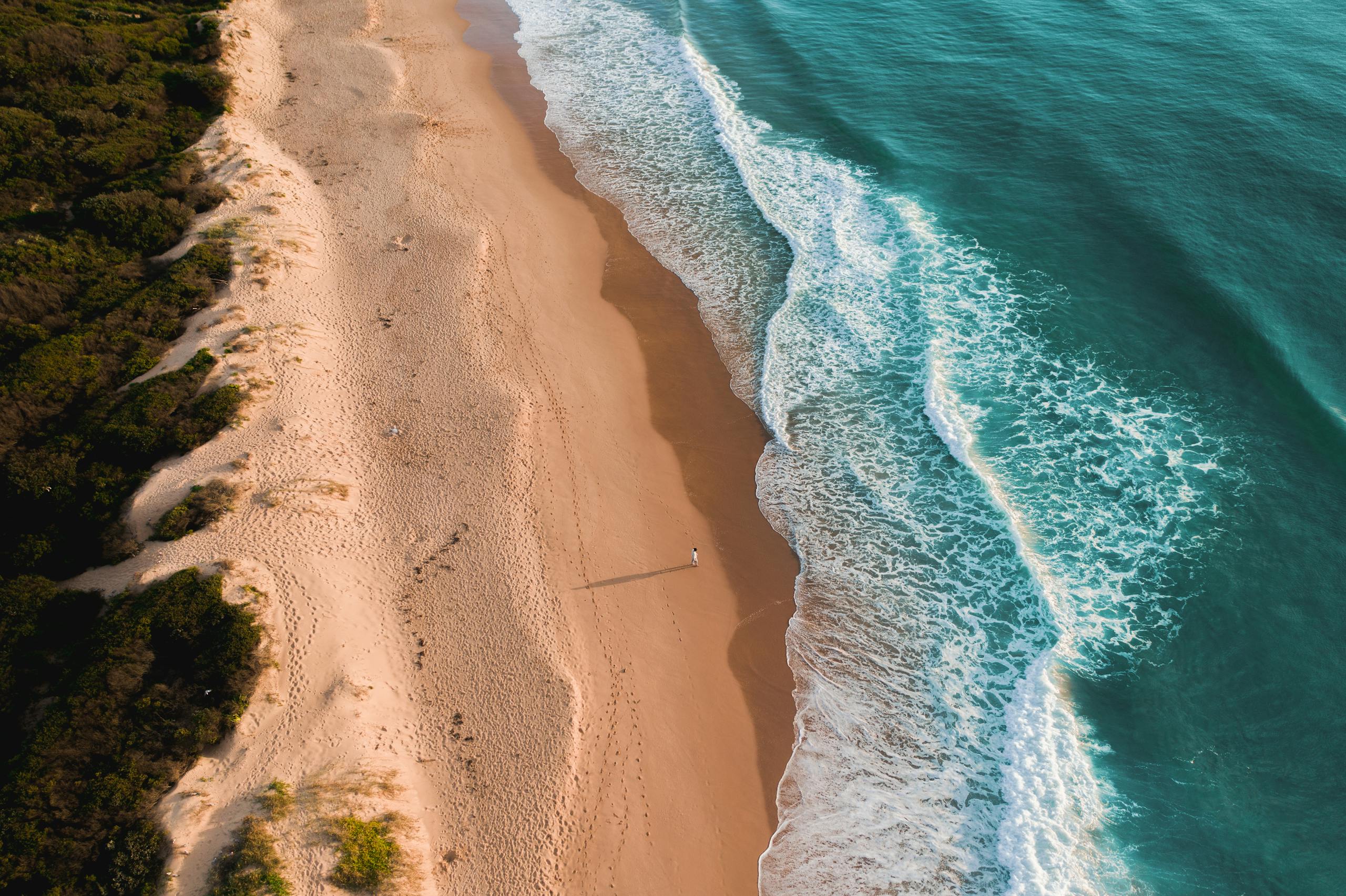 Aerial view of blue wavy ocean washing sandy beach with rocky formations in sunny day