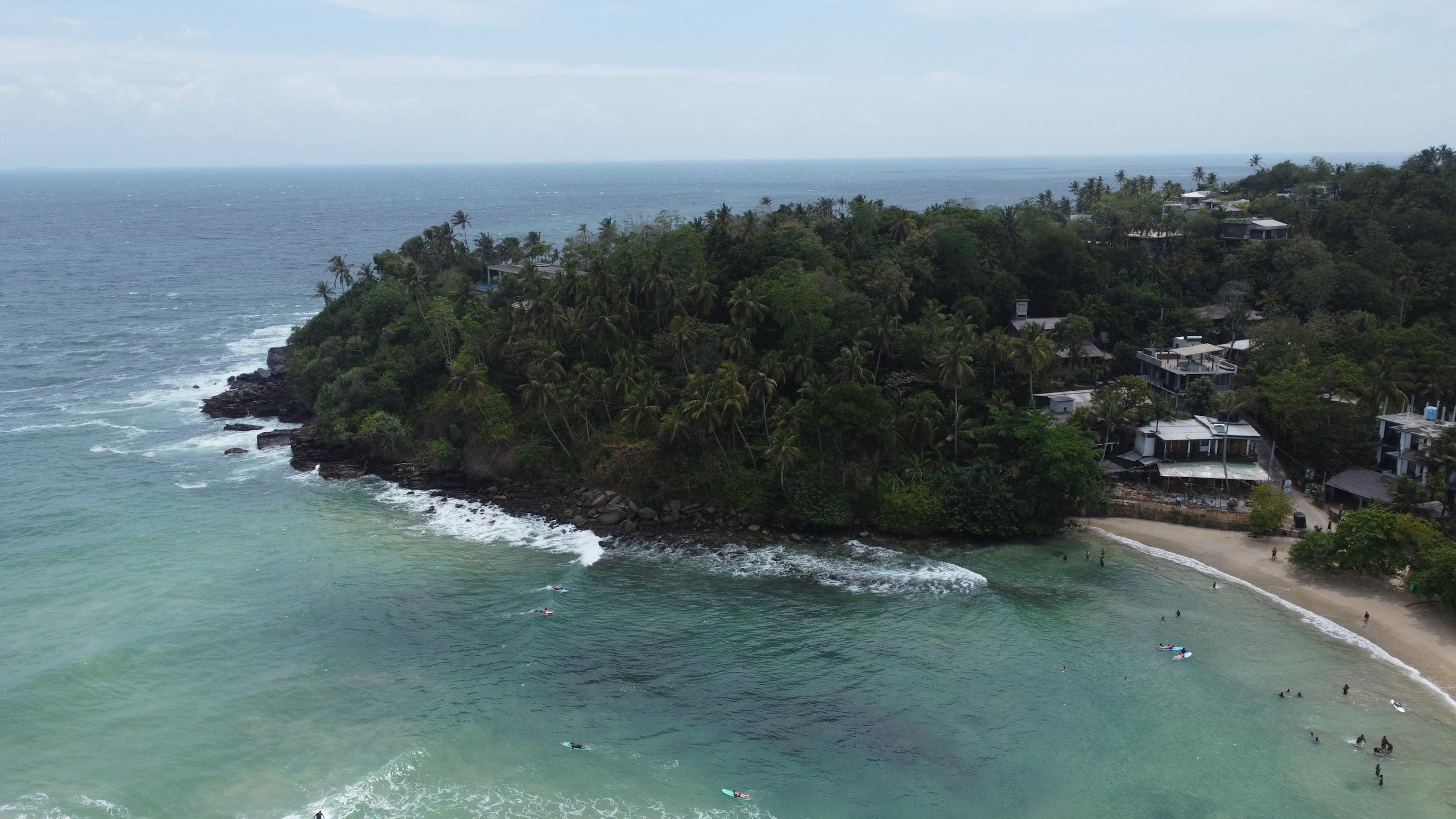 Drone shot capturing the beautiful coastline of Hiriketiya Beach, Sri Lanka, with lush greenery and clear blue waters.