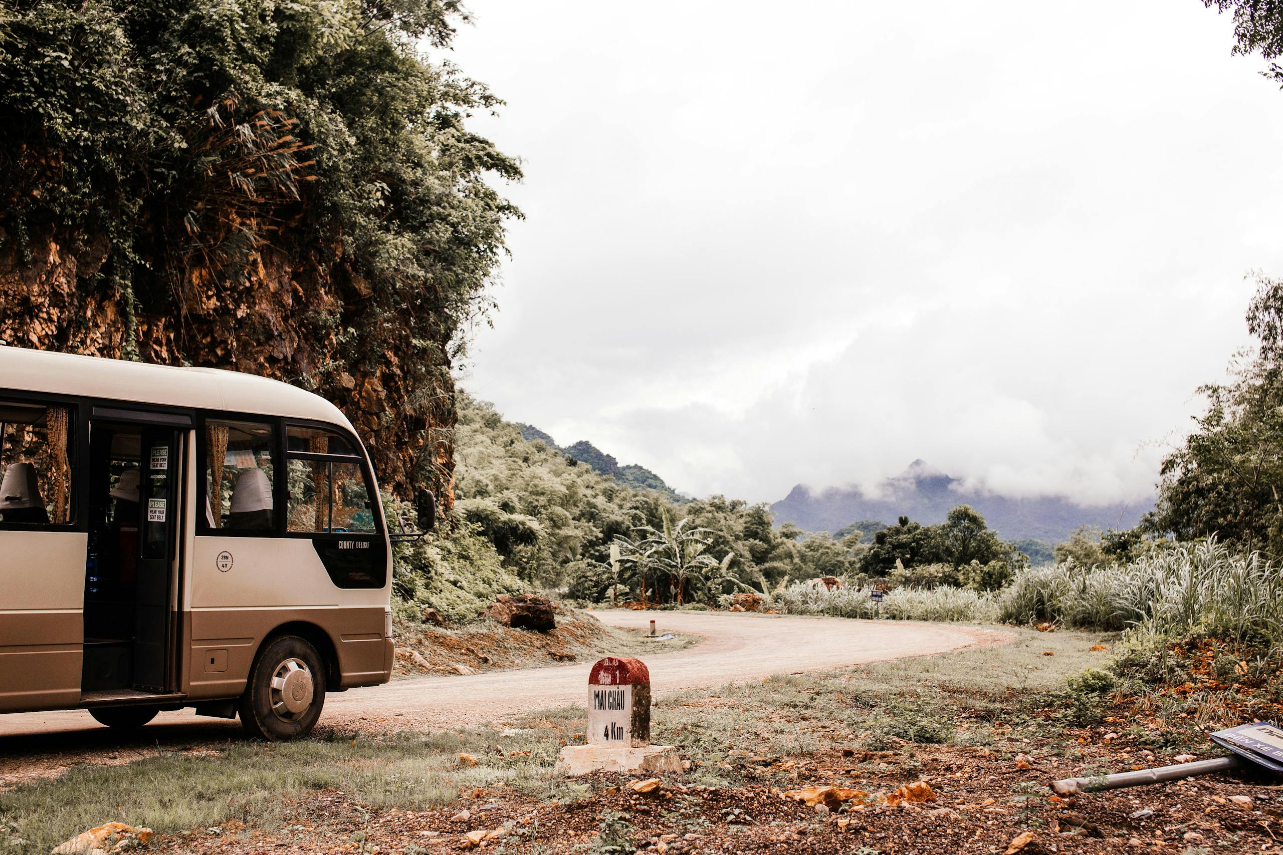 Shuttle bus on a winding road with mountainous backdrop and lush greenery.