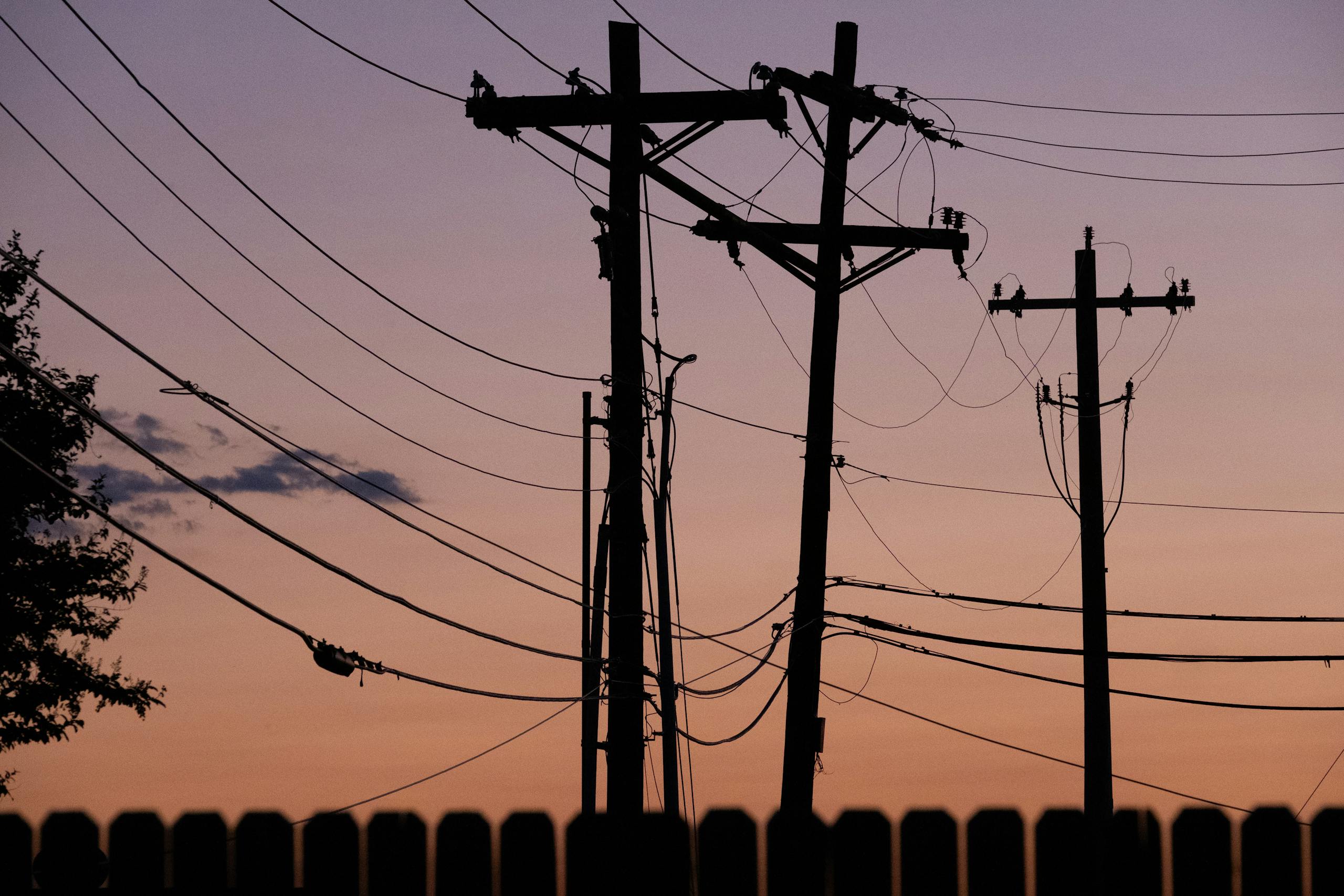 Silhouetted power lines and poles against a vibrant sunset sky, conveying energy and connectivity.