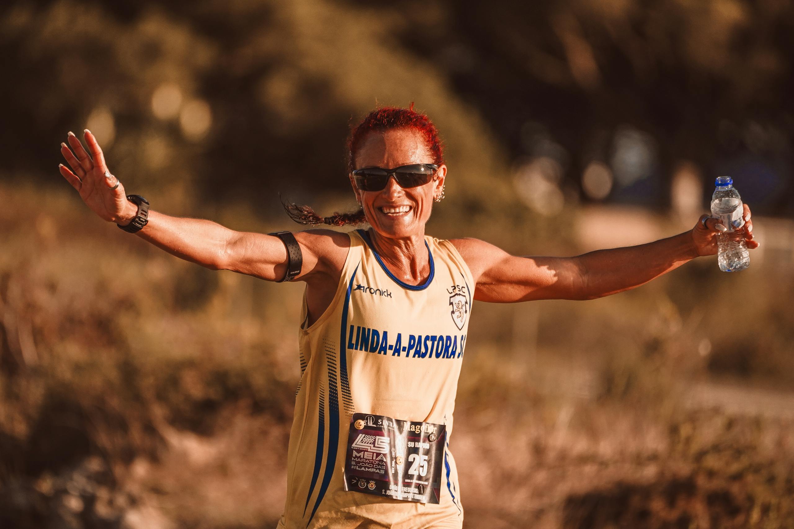 Smiling woman with sunglasses celebrates marathon victory outdoors.