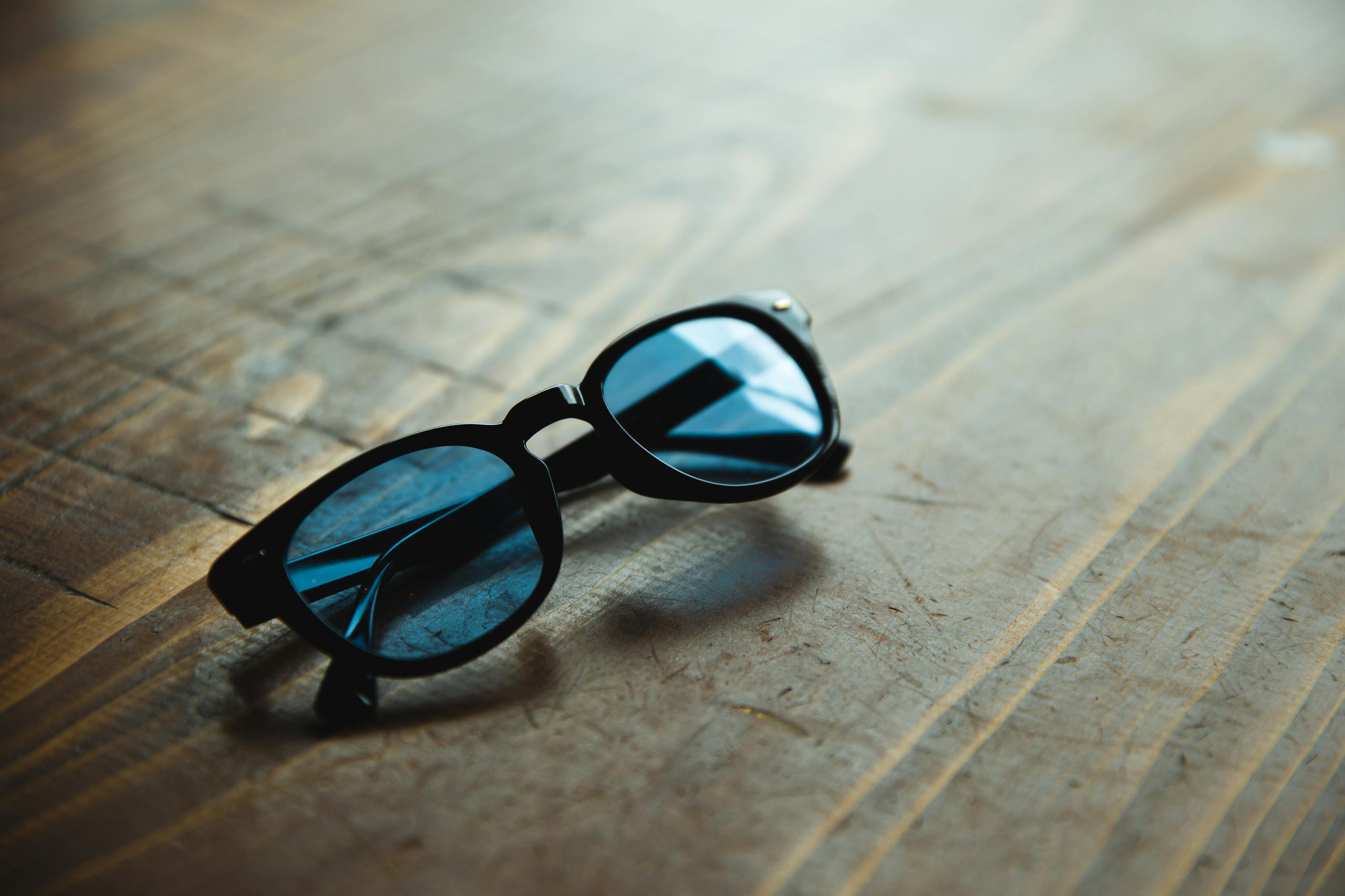 Stylish sunglasses with blue glass and black frames placed on shabby wooden table in daylight