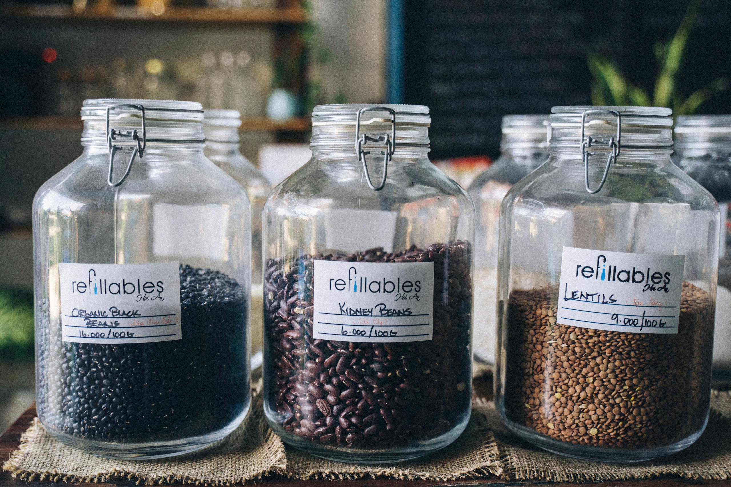 Three refillable glass jars with organic black beans, kidney beans, and lentils in a shop setting.