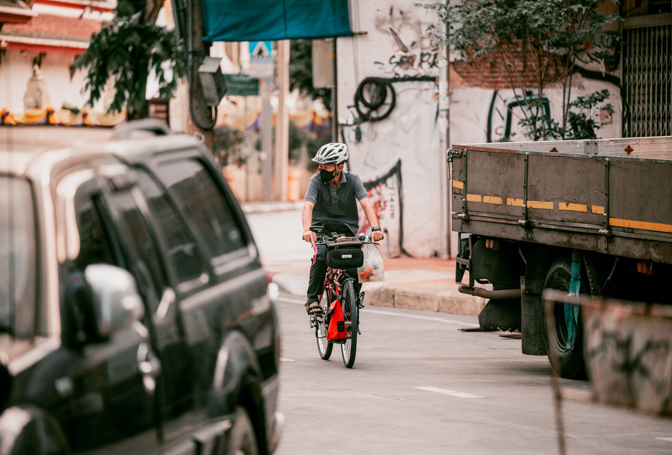 A cyclist rides through a busy urban street in Bangkok, surrounded by vehicles and graffiti.
