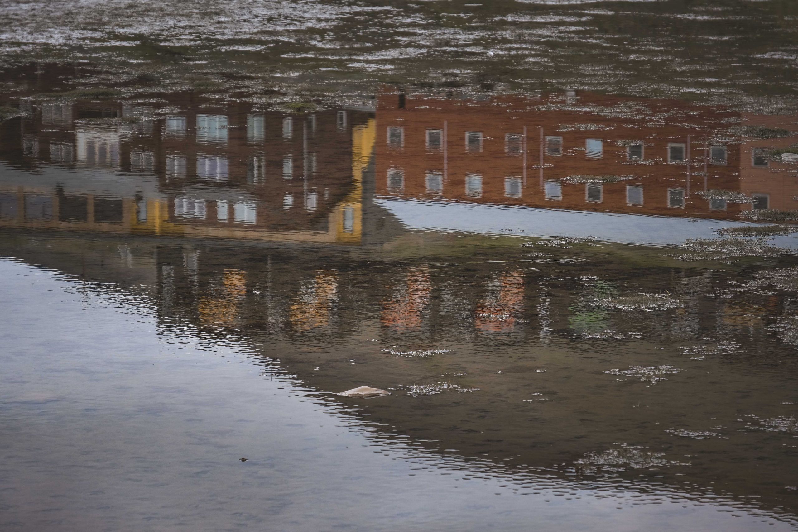 Captivating reflection of brown brick buildings mirrored in a calm water surface.