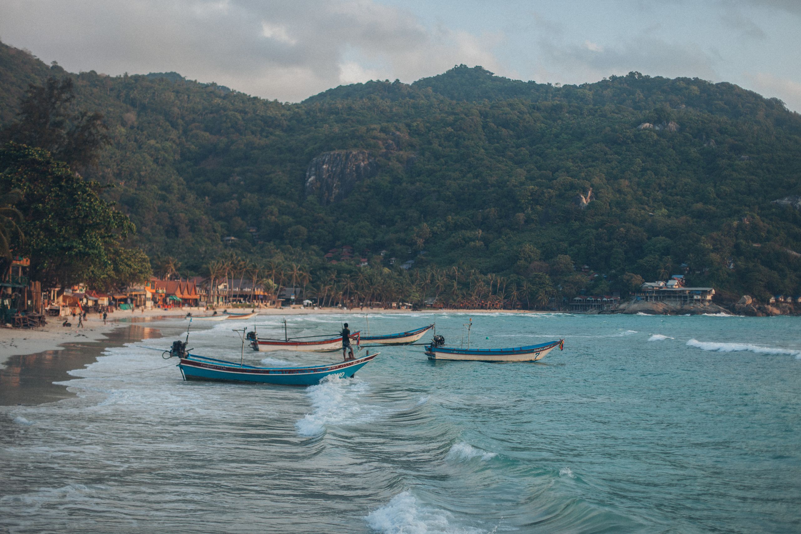 Panoramic view of boats by the shore against lush green hills and gentle waves under a clear sky.