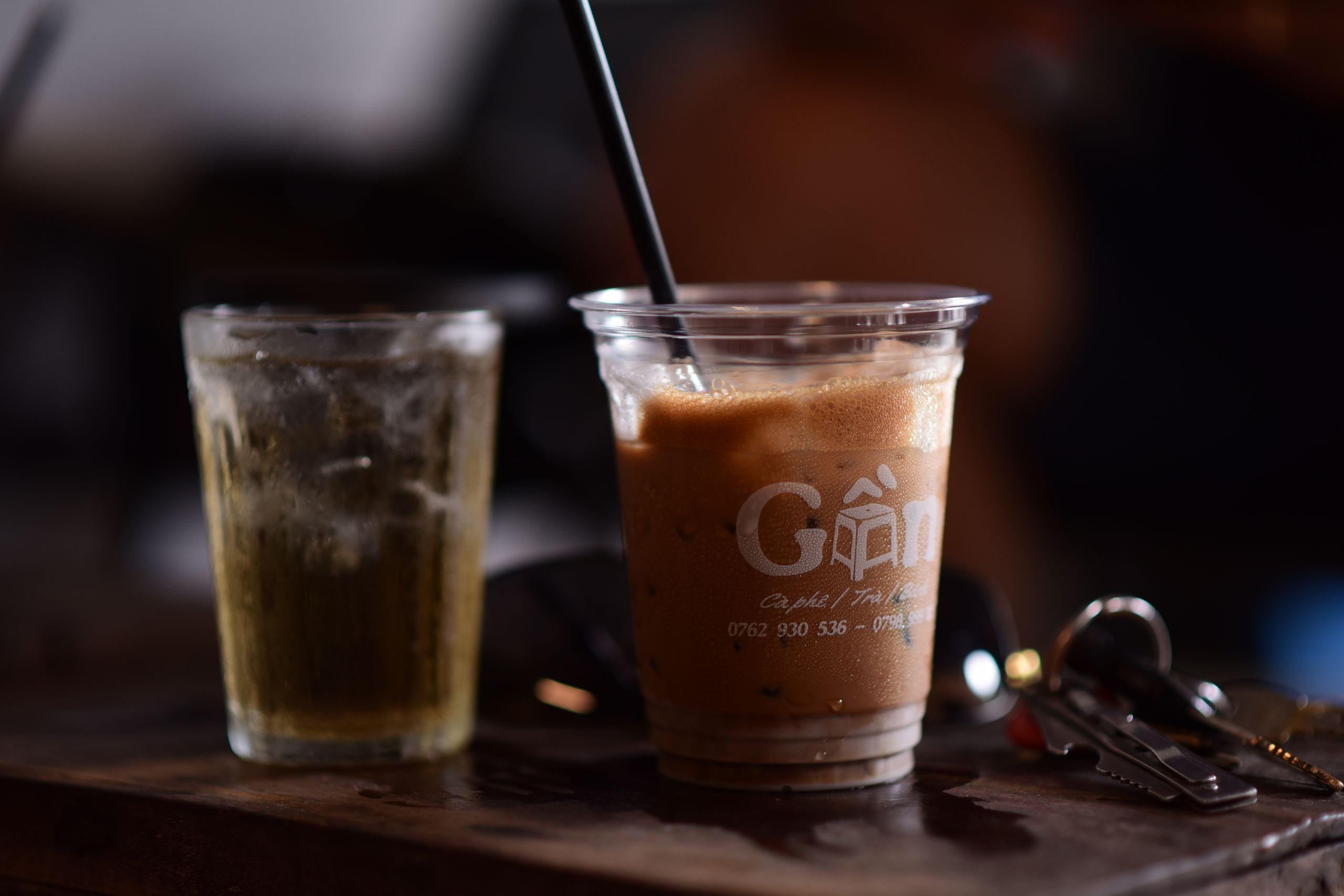 Close-up of iced coffee and cold brew beside keys, capturing a casual cafe vibe.