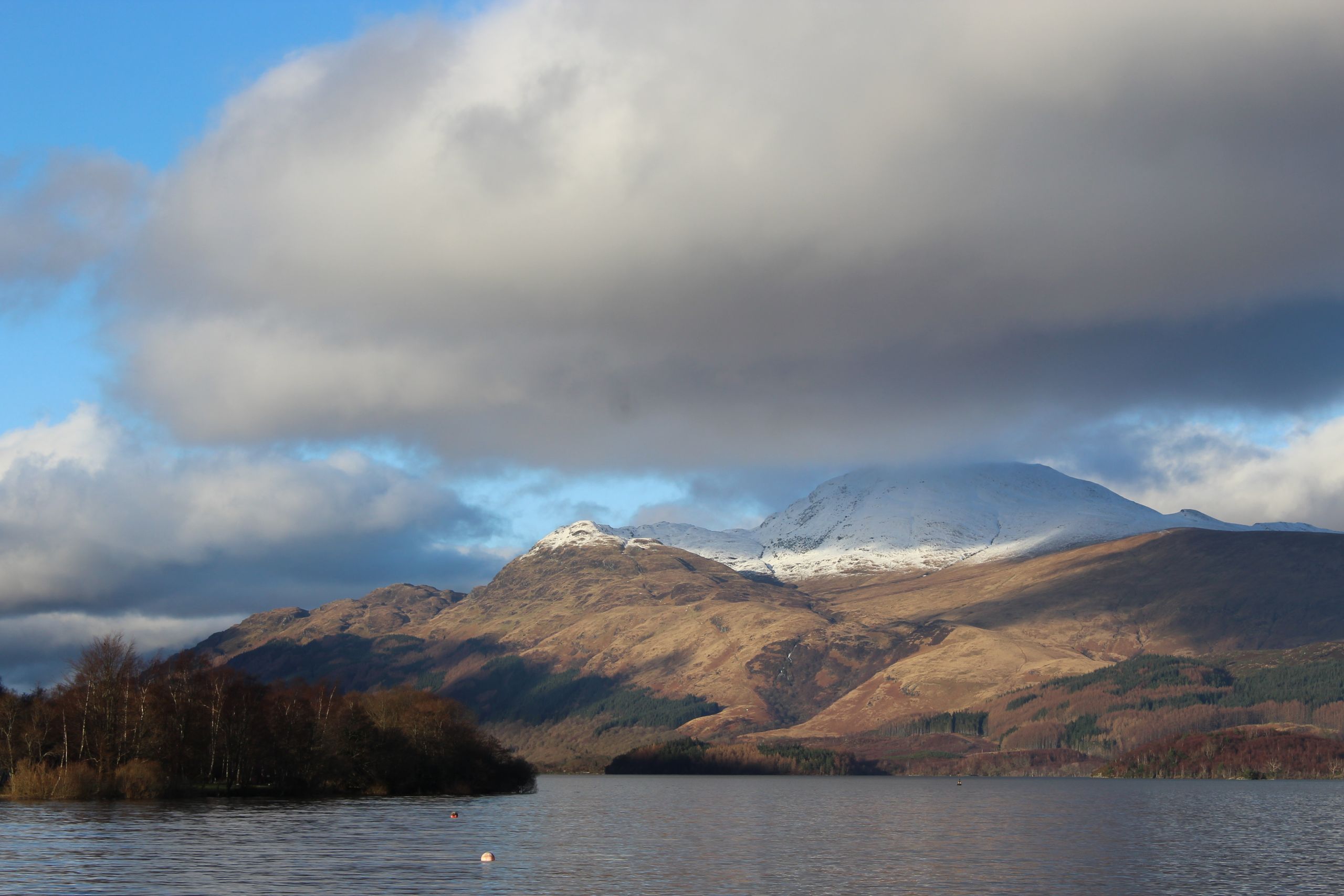 Majestic landscape featuring snow-capped mountains, a tranquil lake, and a dramatic sky.