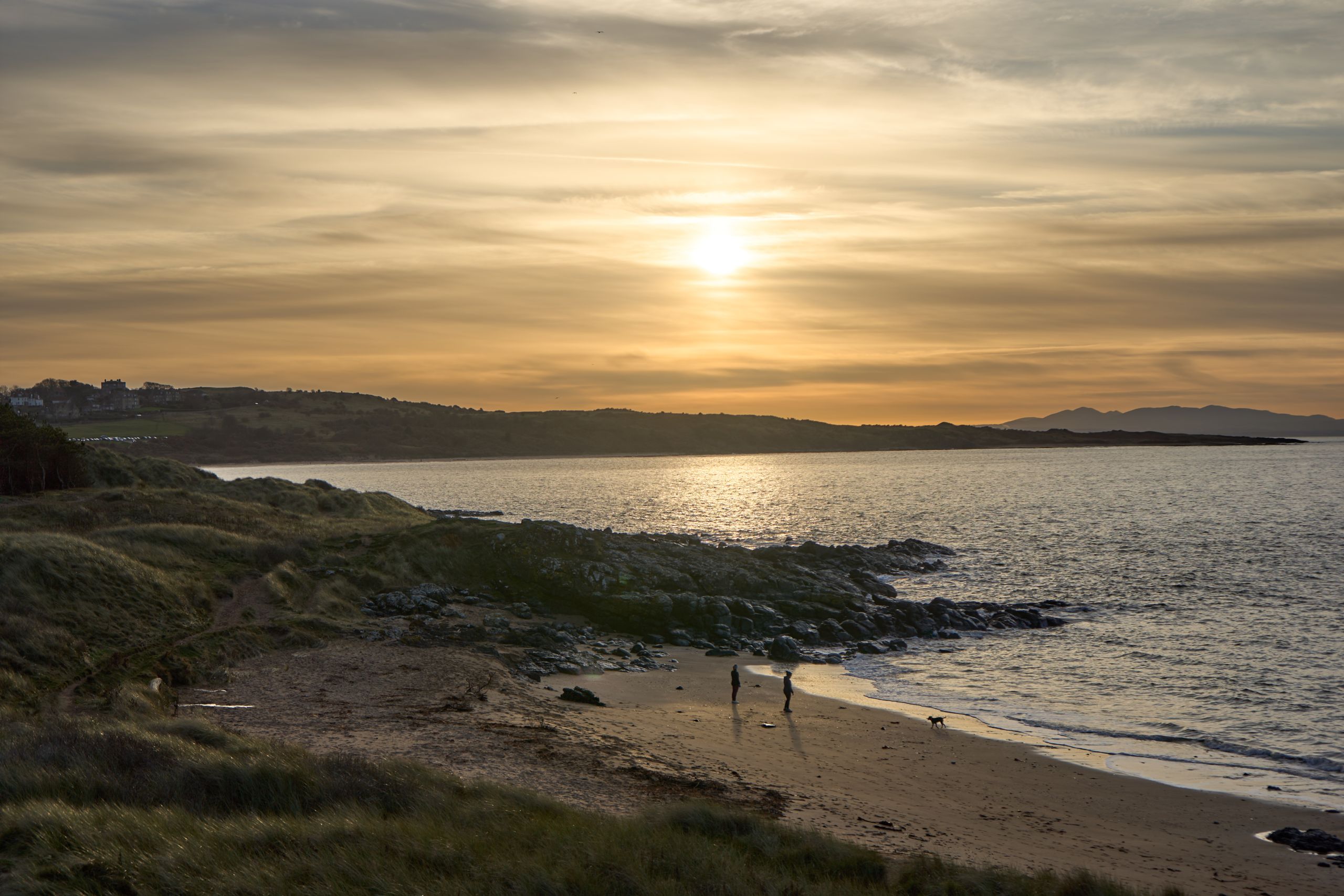 Sunset over a tranquil beach with people and a dog in Gullane, Scotland.