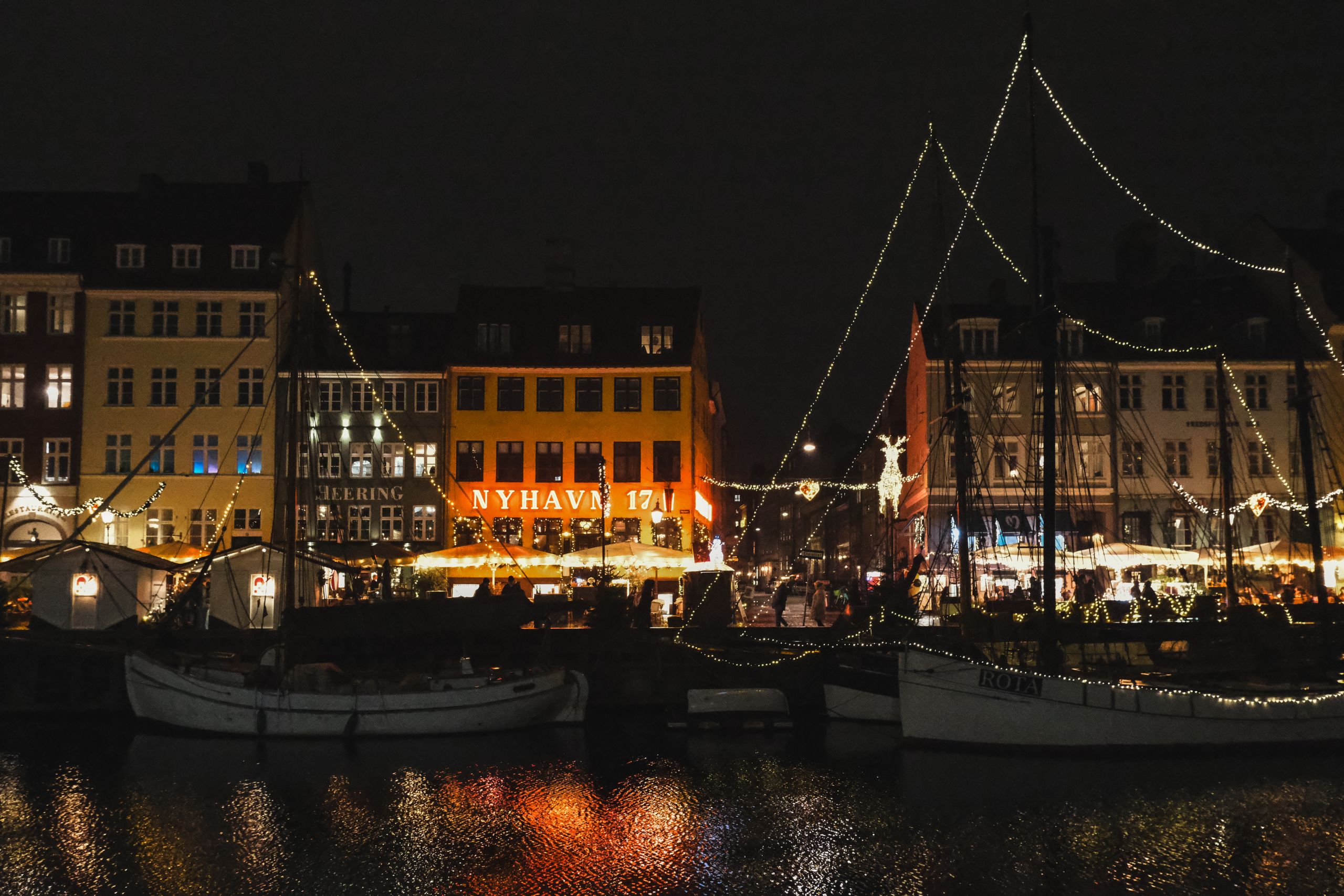 Captivating night scene of Nyhavn Copenhagen with festive lights reflecting on the water.