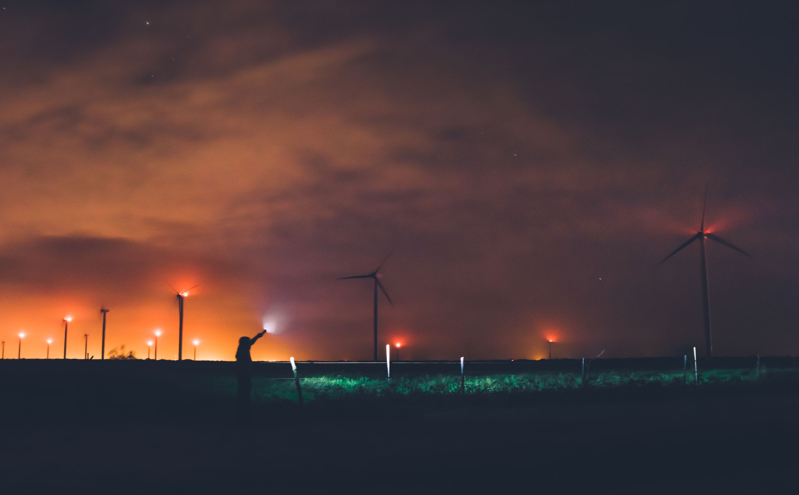 Silhouette of a person near wind turbines at night under cloudy sky in Texas.