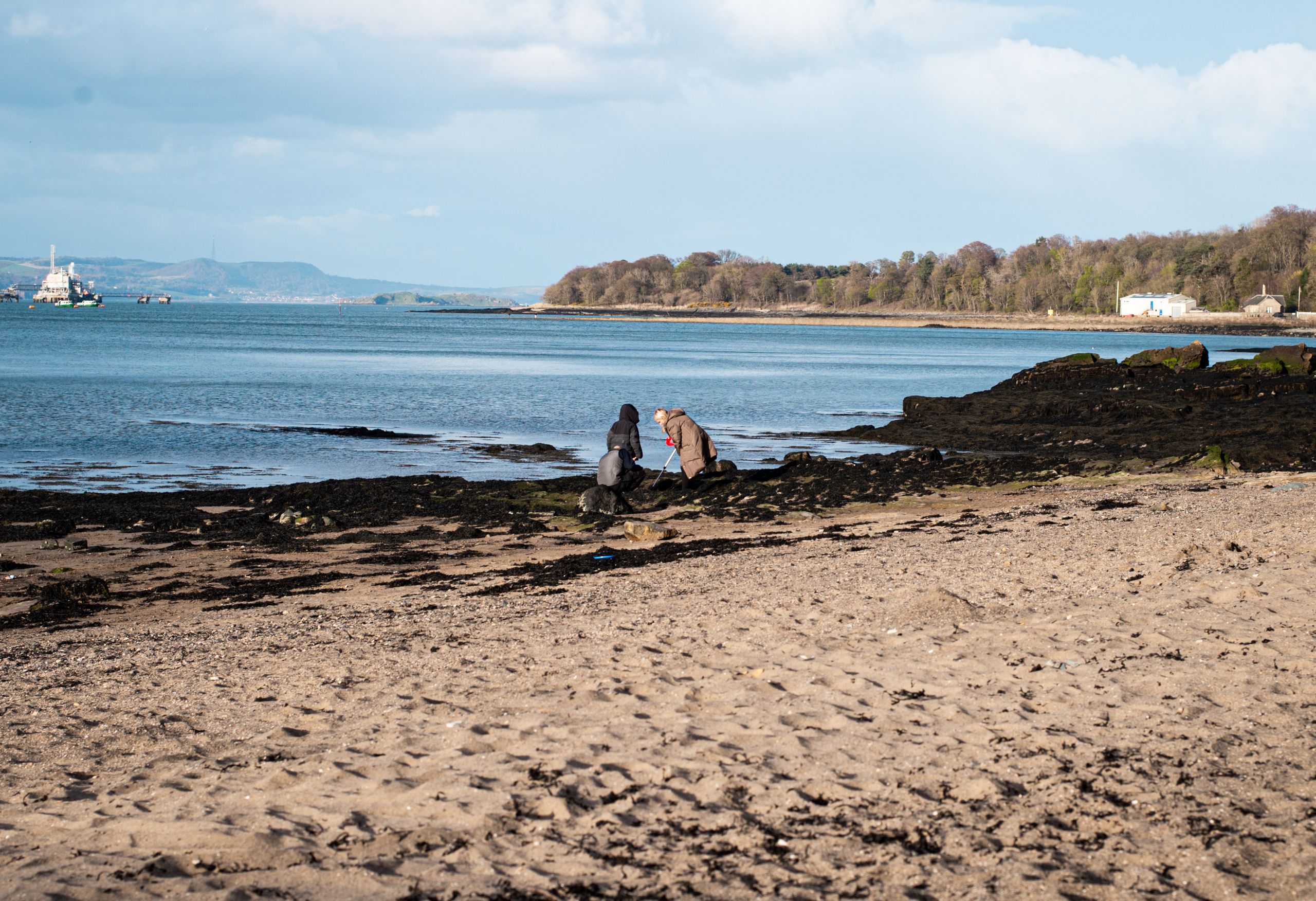Two adults enjoying a serene afternoon at a rocky beach under a clear sky.